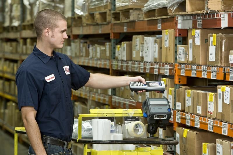 Man in blue shirt scans product from a warehouse shelf using handheld barcode scanner